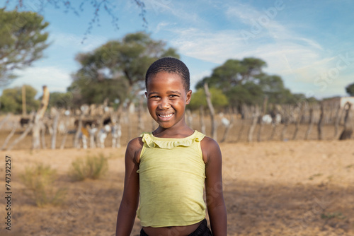 african village child on a dirt road , kraal with small livestock grazing in the background, photo