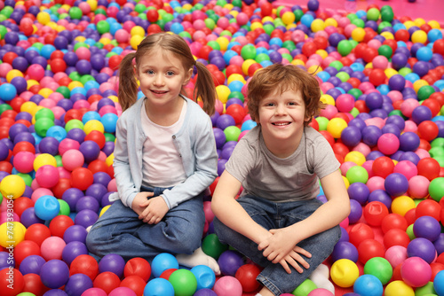 Happy little kids sitting on colorful balls in ball pit