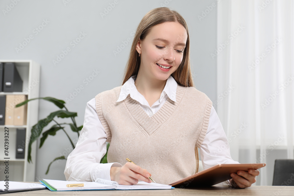 Woman taking notes while using tablet at table in office Woman taking notes while using tablet at table in office