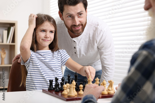 Family playing chess together at table in room