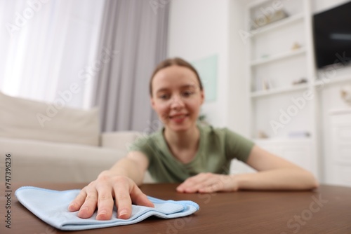 Woman with microfiber cloth cleaning wooden table in room, selective focus