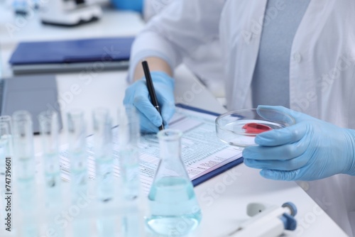 Laboratory worker holding petri dish with blood sample while working at white table  closeup