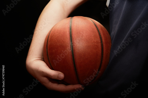 A hand holds a lit basketball near the hip on a black background, close-up, the start of the game, the start of training. © Александр Ланевский