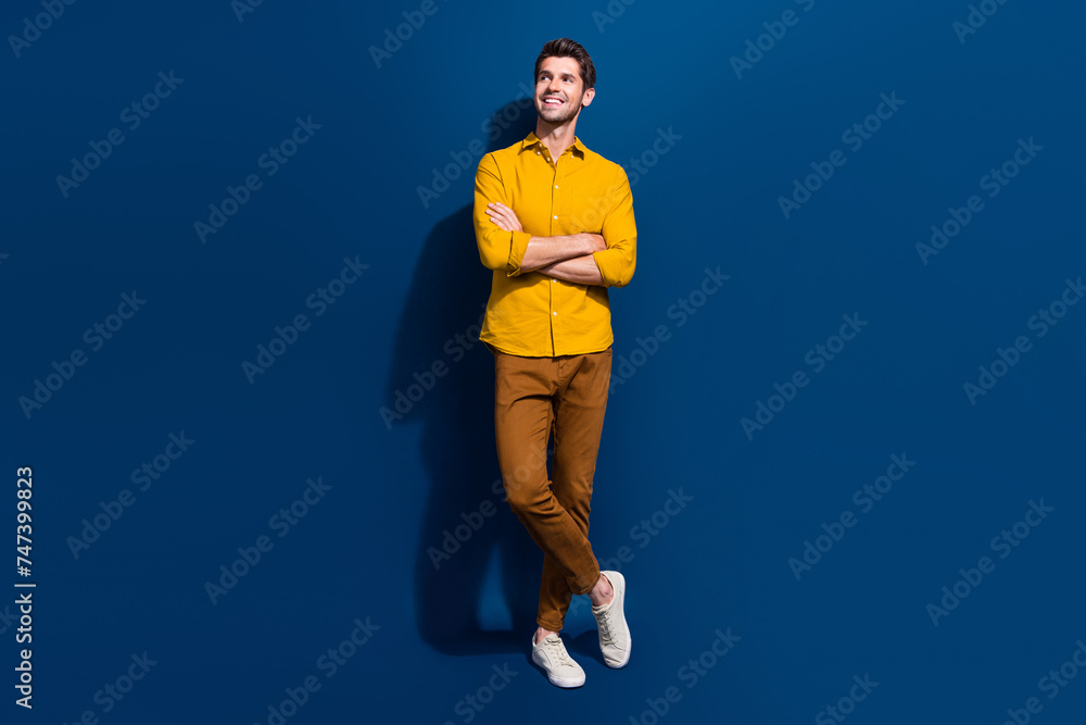 Full body photo of handsome young guy folded hands look empty space dressed stylish yellow outfit isolated on dark blue color background Full body photo of handsome young guy folded hands look empty space dressed stylish yellow outfit isolated on dark blue color background