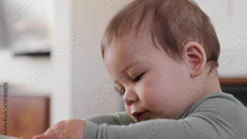 Baby boy plays with food on his placemat with avocado on his face