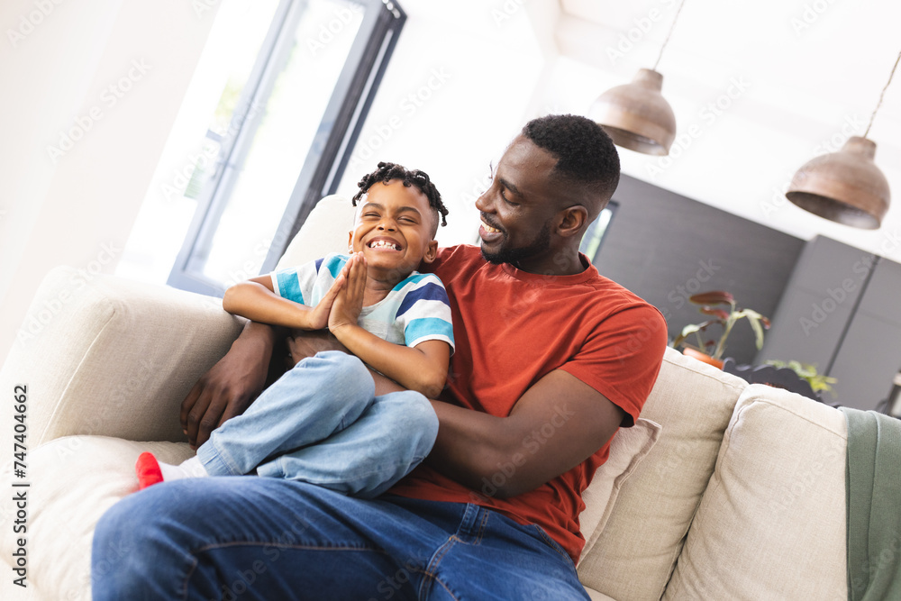 African American father and son share a joyful moment on a sofa African American father and son share a joyful moment on a sofa
