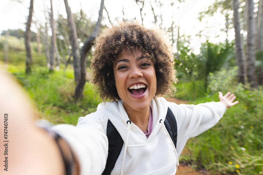 Young biracial woman with curly hair takes a selfie, arms outstretched ...