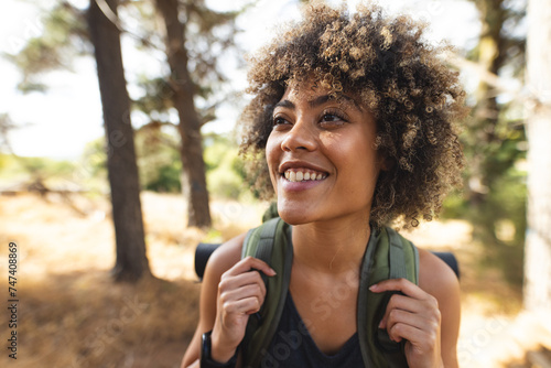 A young biracial woman with curly hair smiles while hiking in a forest photo