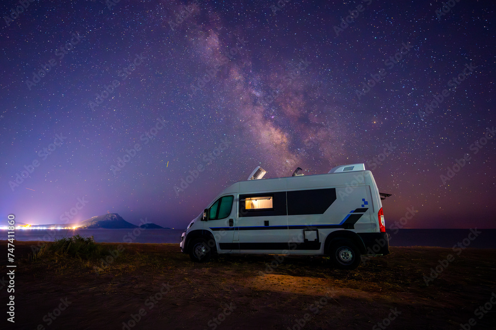 Campervan or motorhome parked on the beach in Greece under the stars and milky way. Tourists enjoying and relaxing on the beach with RV campervan on family vacation.