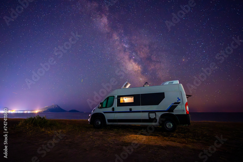 Campervan or motorhome parked on the beach in Greece under the stars and milky way. Tourists enjoying and relaxing on the beach with RV campervan on family vacation.