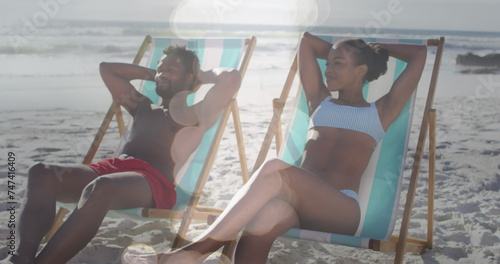 Image of dots over happy african american couple lying on sunbeds on beach