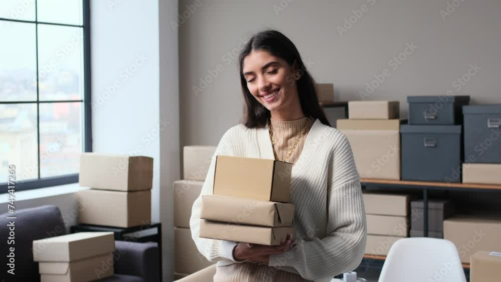 Portrait of a happy Caucasian woman, online store owner, looking at camera and holding cardboard boxes or consumers parcels in warehouse office. Copy space. Portrait of a happy Caucasian woman, online store owner, looking at camera and holding cardboard boxes or consumers parcels in warehouse office. Copy space.
