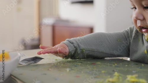 Baby boy plays with food on his placemat with avocado on his face