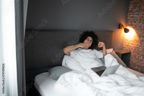 Young man lying in bed , stretching and feeling sleepy