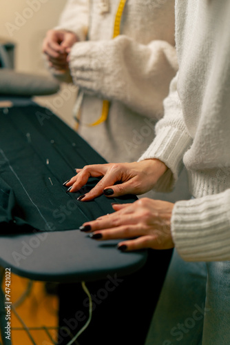close up in a sewing workshop a seamstress pins a corrugated pin on a black fabric © Guys Who Shoot