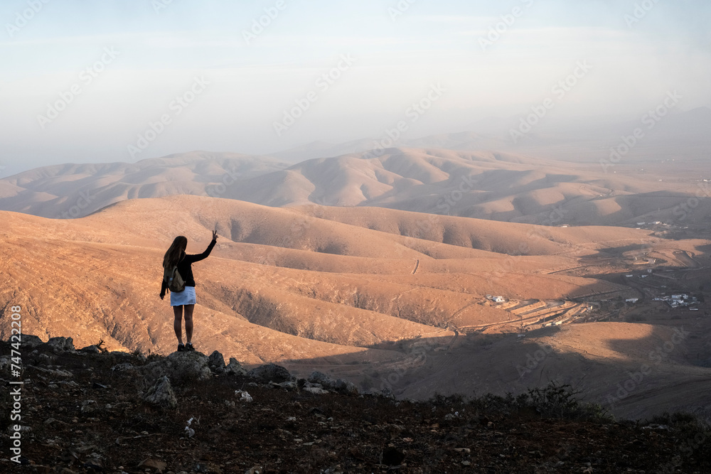 Una mujer visitando el mirador en Fuerteventura y disfrutando de la grandeza de las montañas áridas y bonitas - obrazy, fototapety, plakaty 