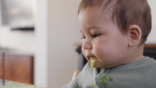 Baby boy plays with food on his placemat with avocado on his face
