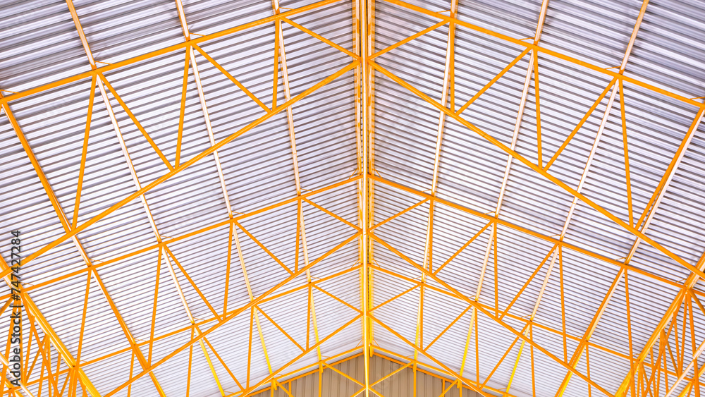 Geometric pattern background of yellow metal roof beams with aluminum corrugated tile roof of industrial warehouse building, low angle and symmetric view