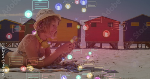 Image of social media icon over caucasian woman with phone on beach