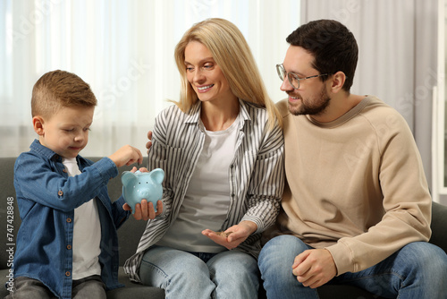 Fototapeta Naklejka Na Ścianę i Meble -  Family budget. Little boy putting coin into piggy bank and his parents at home
