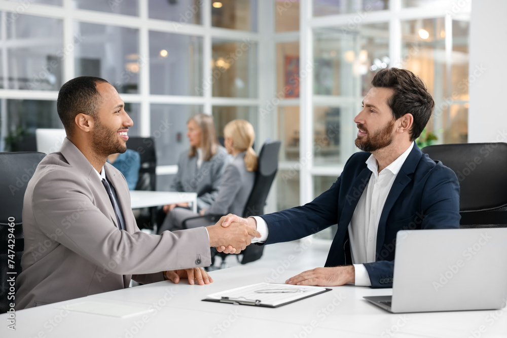 Lawyer shaking hands with client at table in office, selective focus Lawyer shaking hands with client at table in office, selective focus