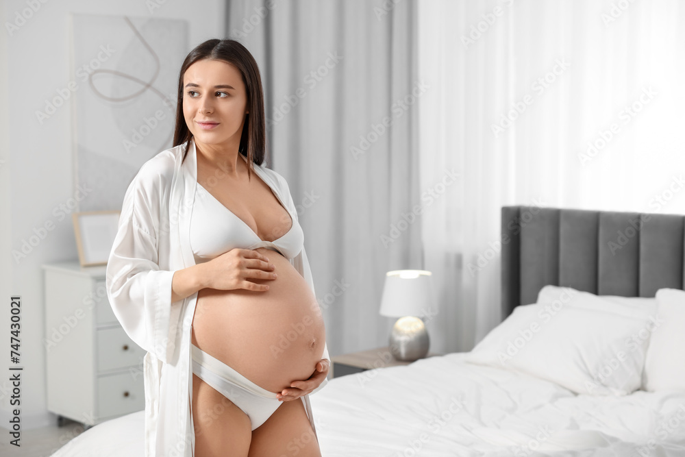 Beautiful pregnant woman wearing stylish comfortable underwear and robe in bedroom, space for text Beautiful pregnant woman wearing stylish comfortable underwear and robe in bedroom, space for text