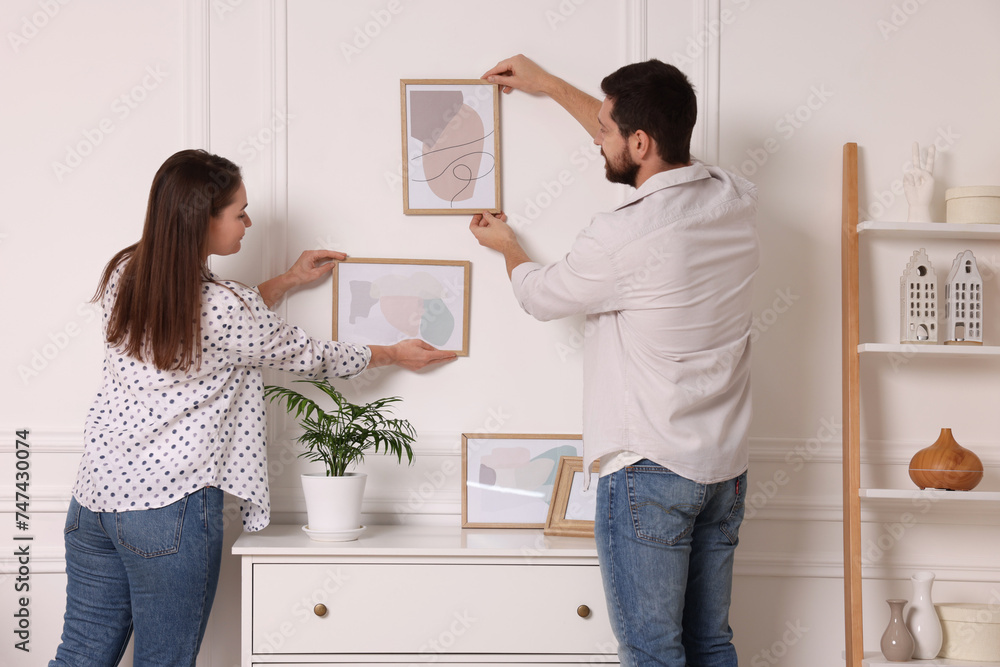 Man and woman hanging picture frames on white wall at home Man and woman hanging picture frames on white wall at home