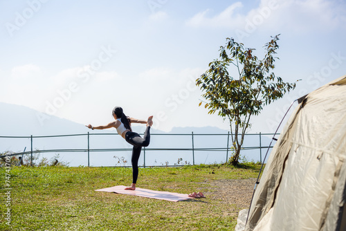 Woman do yoga exercise in camp site with camping tent