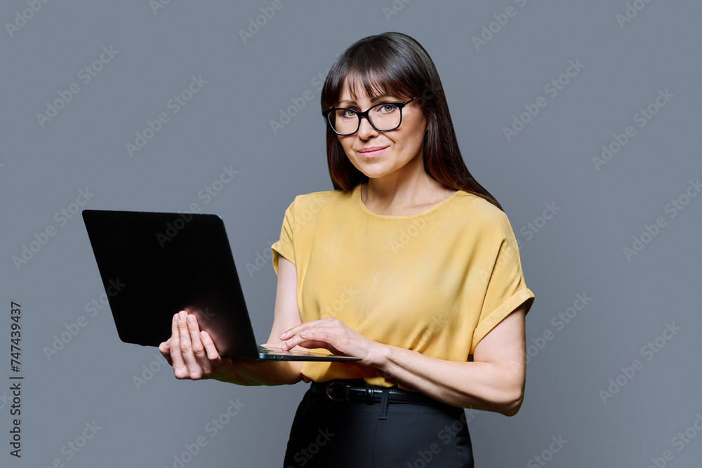 Middle-aged business confident woman using laptop on gray background Middle-aged business confident woman using laptop on gray background