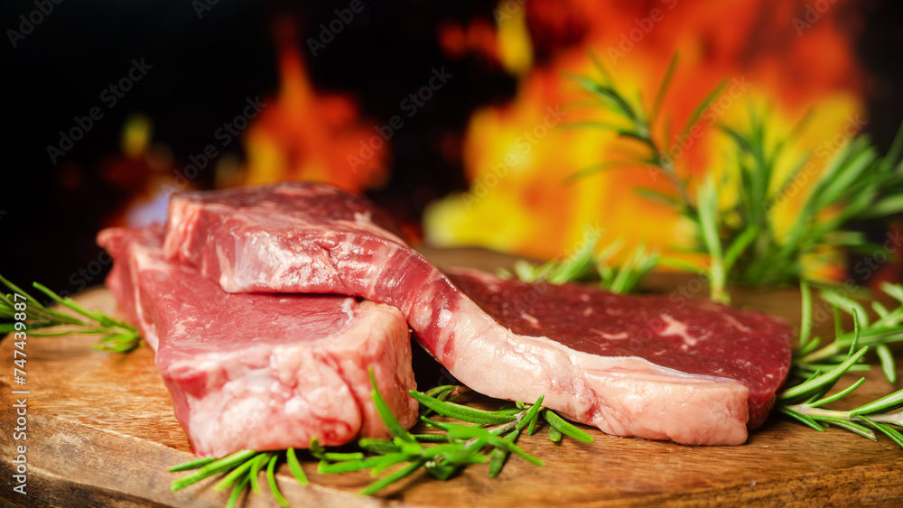 Fresh Raw Steak on Wooden Board with Rosemary in Front of a Blazing Fire