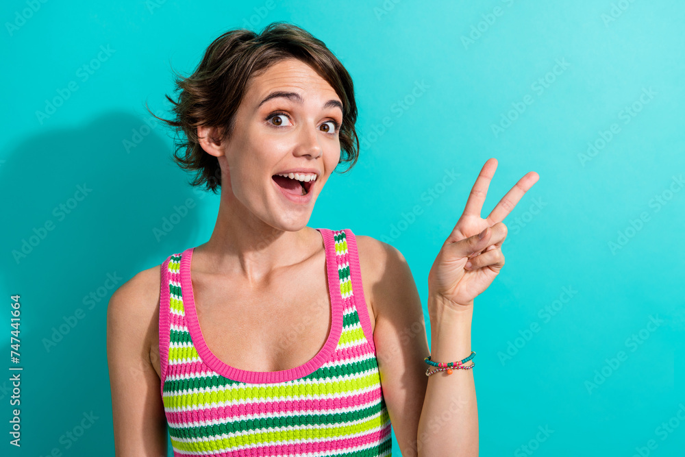 Portrait of pretty funny lady showing v sign symbol greet friends good mood wear striped singlet isolated teal color background Portrait of pretty funny lady showing v sign symbol greet friends good mood wear striped singlet isolated teal color background