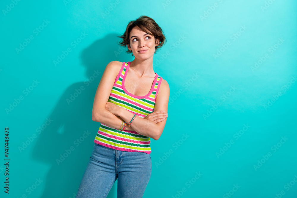 Portrait of pretty young lady holding arms crossed looking empty space wear striped top blue jeans isolated teal color background Portrait of pretty young lady holding arms crossed looking empty space wear striped top blue jeans isolated teal color background