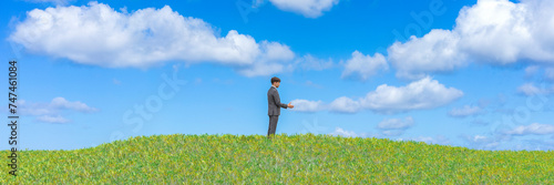 Solitude in Serenity: Man in Suit Standing Alone on a Lush Green Hill Under Blue Sky