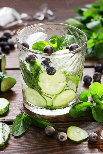 Cucumber and blueberry flavored with mint water or alcohol tonic cocktail on wooden table on dark background, vertical, fresh spring and summer detox drinks, natural healthy food concept