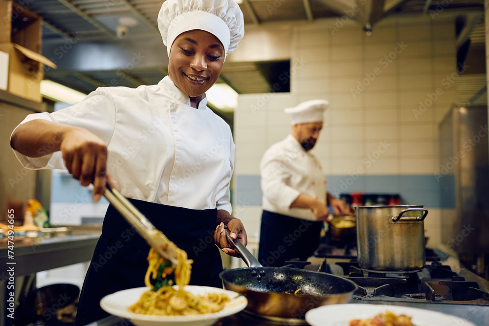 Happy black female chef serving food while working in restaurant kitchen. Happy black female chef serving food while working in restaurant kitchen.