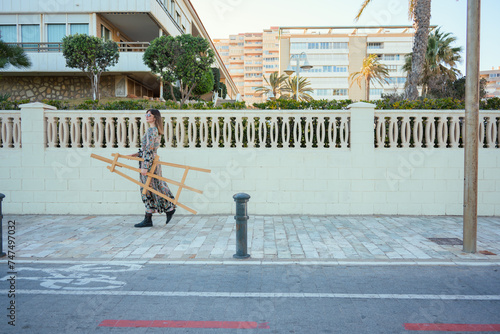 Woman Walking Down Sidewalk Next to Tall Building with a Easel