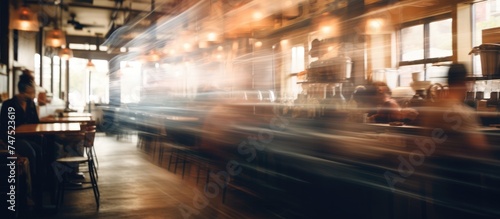 In this blurry image, a group of individuals can be seen sitting at a table inside a coffee shop or restaurant. Some are conversing, while others appear to be eating or drinking. © Vusal