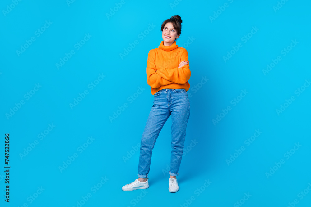 Full length photo of cheerful dreamy woman dressed orange sweater arms crossed looking empty space isolated blue color background Full length photo of cheerful dreamy woman dressed orange sweater arms crossed looking empty space isolated blue color background