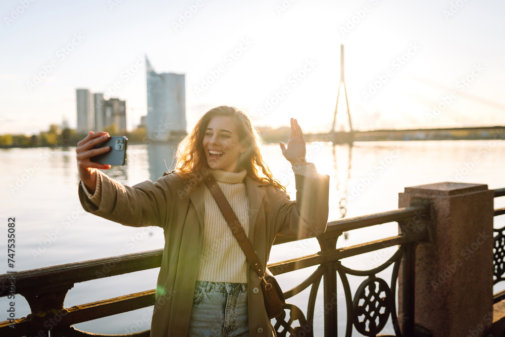 Happy woman with a mobile phone, takes a selfie, communicates with friends, blogs outdoor. Lifestyle, travel, tourism, nature, active life. - obrazy, fototapety, plakaty 