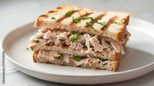 a toast bread sandwich filled with tuna and fresh cheese, cut in half to reveal the filling, presented on a clean white plate.