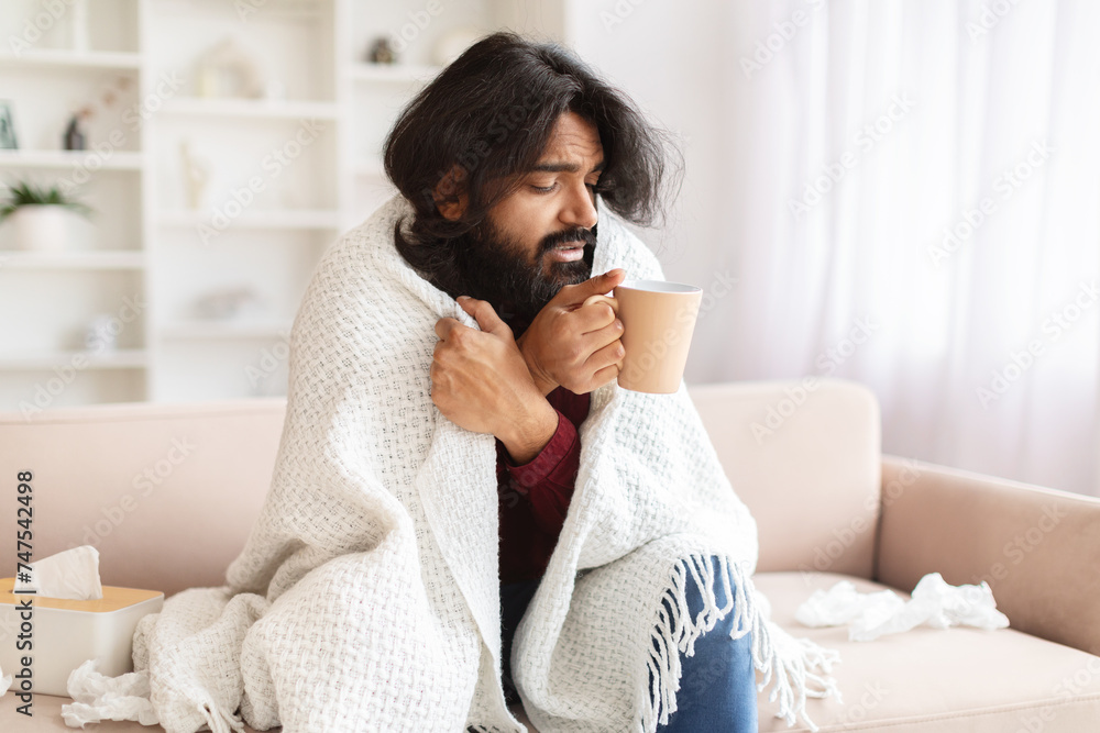 Sick millennial eastern man have cold or flu, drinking warm tea Sick millennial eastern man have cold or flu, drinking warm tea