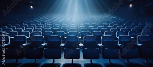 An empty theater illuminated by a bright light coming from the ceiling, showcasing rows of blue-toned chairs and an empty stage. photo
