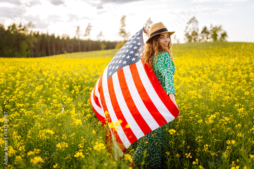 Portrait young woman with American national flag, enjoying sunset at field. 4th of July. Independence Day. Patriotic holiday.