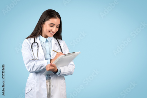 Doctor writing notes on clipboard on light blue backdrop, free space