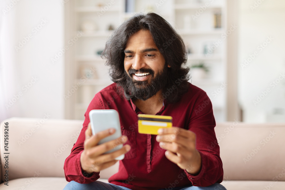 Happy indian man using smartphone and credit card at home Happy indian man using smartphone and credit card at home