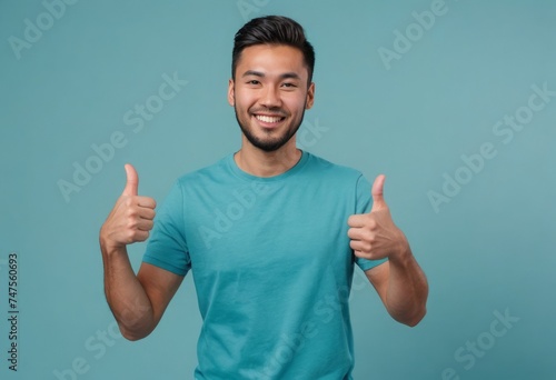 An enthusiastic young man in a turquoise t-shirt giving thumbs up with a bright smile.
