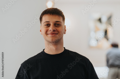 A young adult male with a friendly smile, wearing a casual black t-shirt, poses for a portrait with a softly blurred interior background.