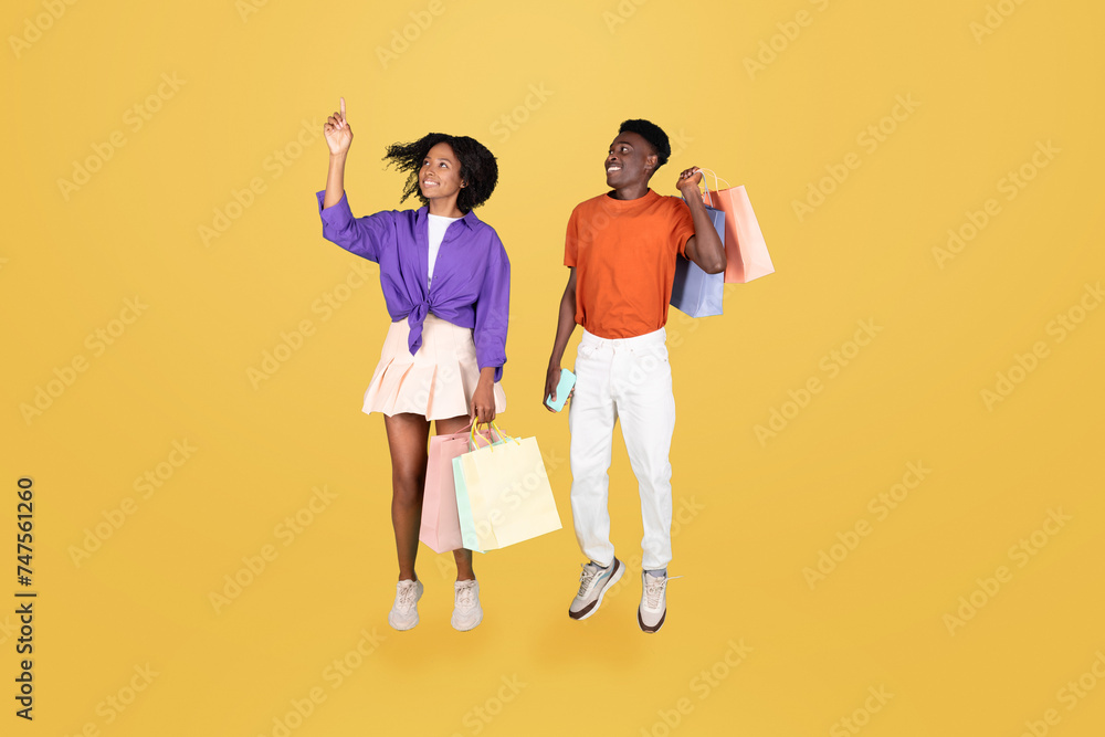 A young woman joyfully points upwards while holding shopping bags A young woman joyfully points upwards while holding shopping bags