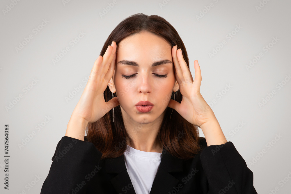 Focused businesswoman in a tailored black suit with closed eyes holds her temples Focused businesswoman in a tailored black suit with closed eyes holds her temples