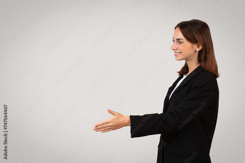 Side profile of a smiling young businesswoman in a black suit extending a handshake Side profile of a smiling young businesswoman in a black suit extending a handshake